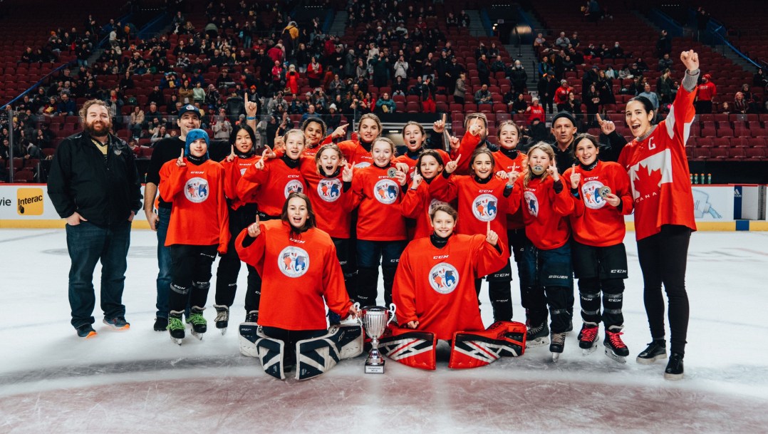 Caroline Ouellette raises her fist in celebration alongside a group of young female hockey players in red jerseys