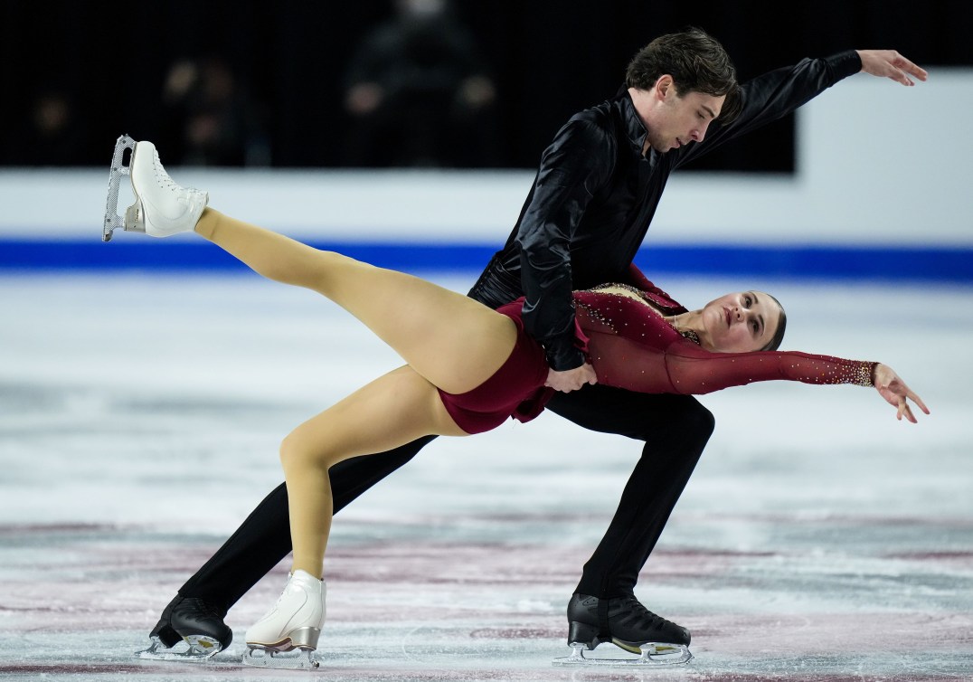 A woman in a burgundy dress and a man in black shirt and pants perform in figure skating 