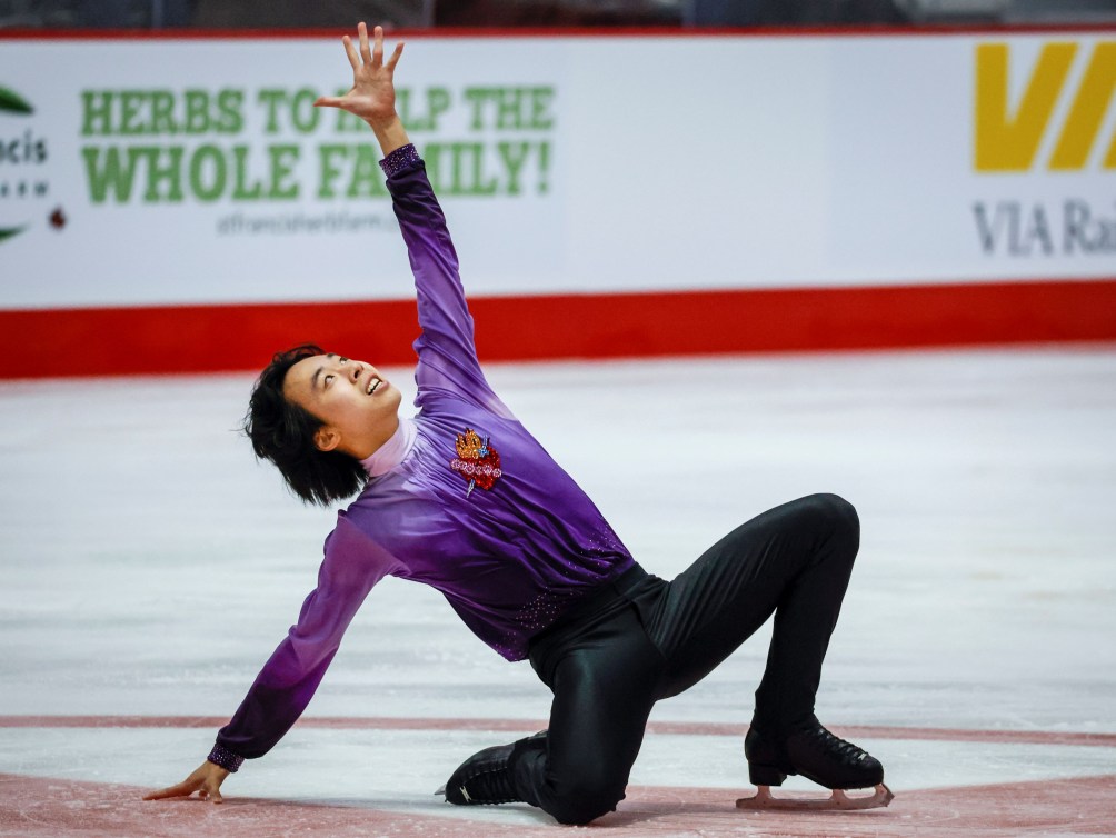 Wesley Chiu in purple shirt and black pants glides across the ice on one knee