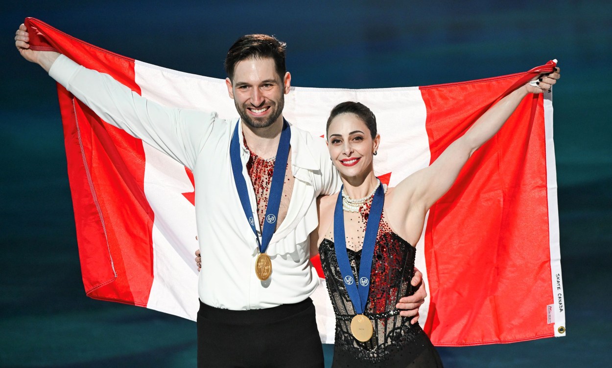 Deanna Stellato-Dudek and Maxime Deschamps hold a Canadian flag behind them while they wear gold medals 