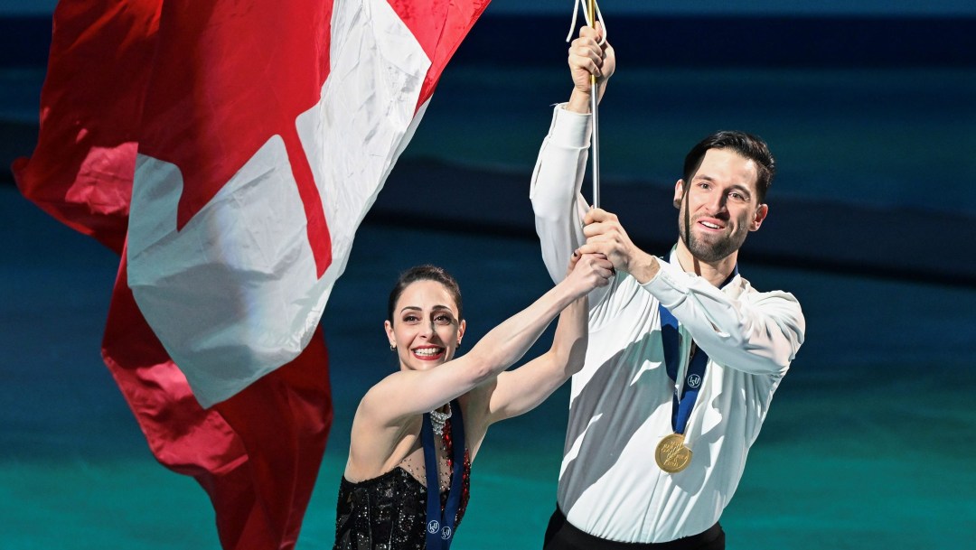 Deanna Stellato-Dudek and Maxime Deschamps carry a big Canadian flag on a pole on a victory lap of the ice