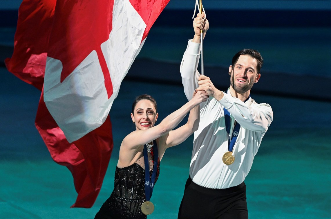 Deanna Stellato-Dudek and Maxime Deschamps carry a big Canadian flag on a pole on a victory lap of the ice 