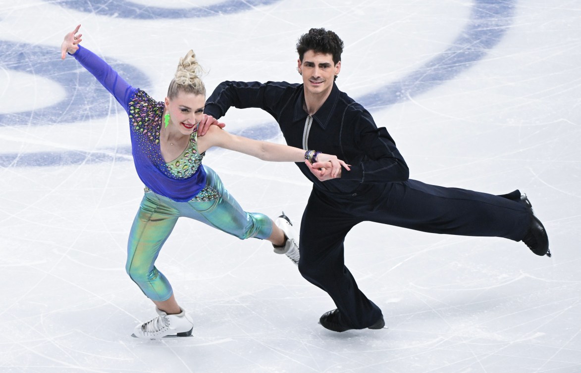 Piper Gilles in a green and purple outfit and Paul Poirier in a black outfit skate side by side 
