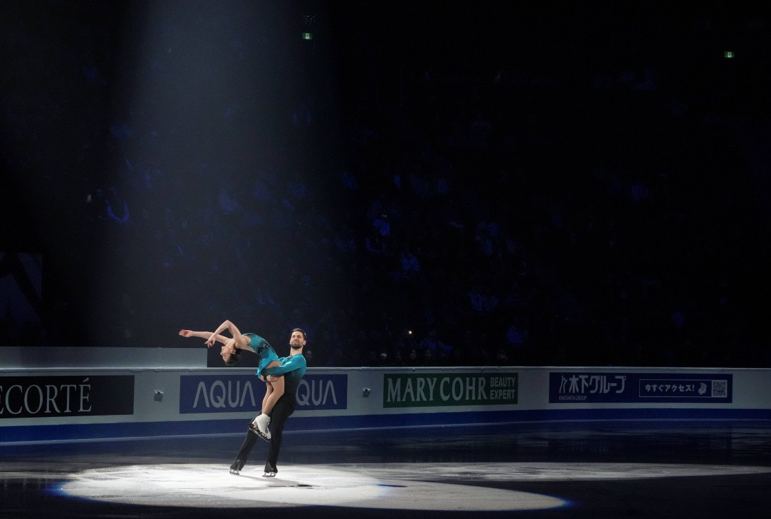 A spotlight follows a duo of pairs skaters as they perform a lift
