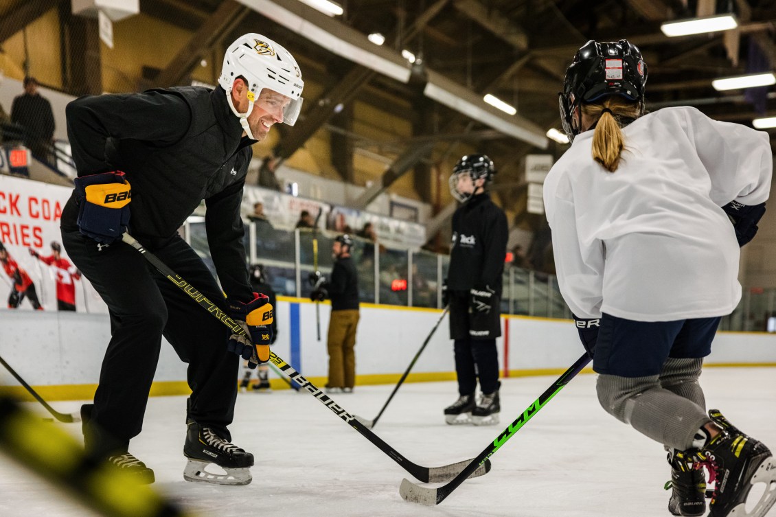 An adult demonstrates a hockey drill to a child
