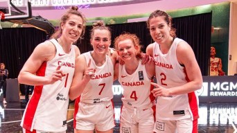 Four women basketball players in white uniforms give a number 1 sign to the camera