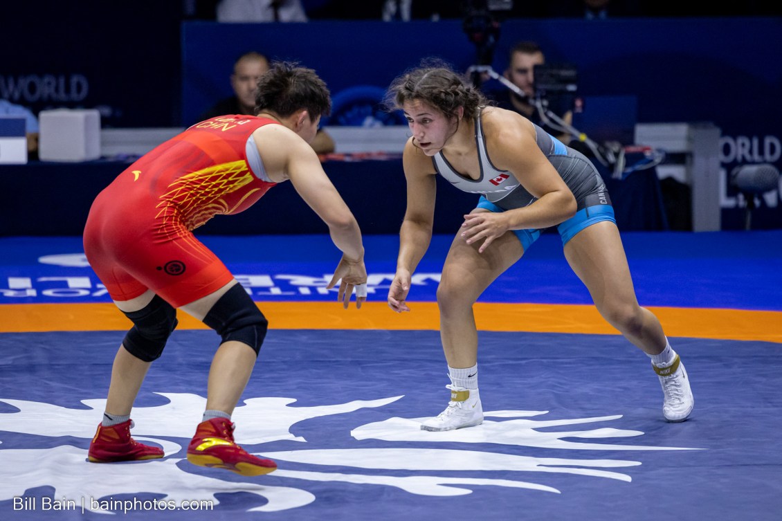 Two female wrestlers are bent at the waist preparing to fight each other on the mat 