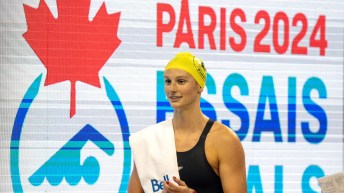 Summer McIntosh walks in front of a board that says Paris 2024 Trials with a towel over her shoulder