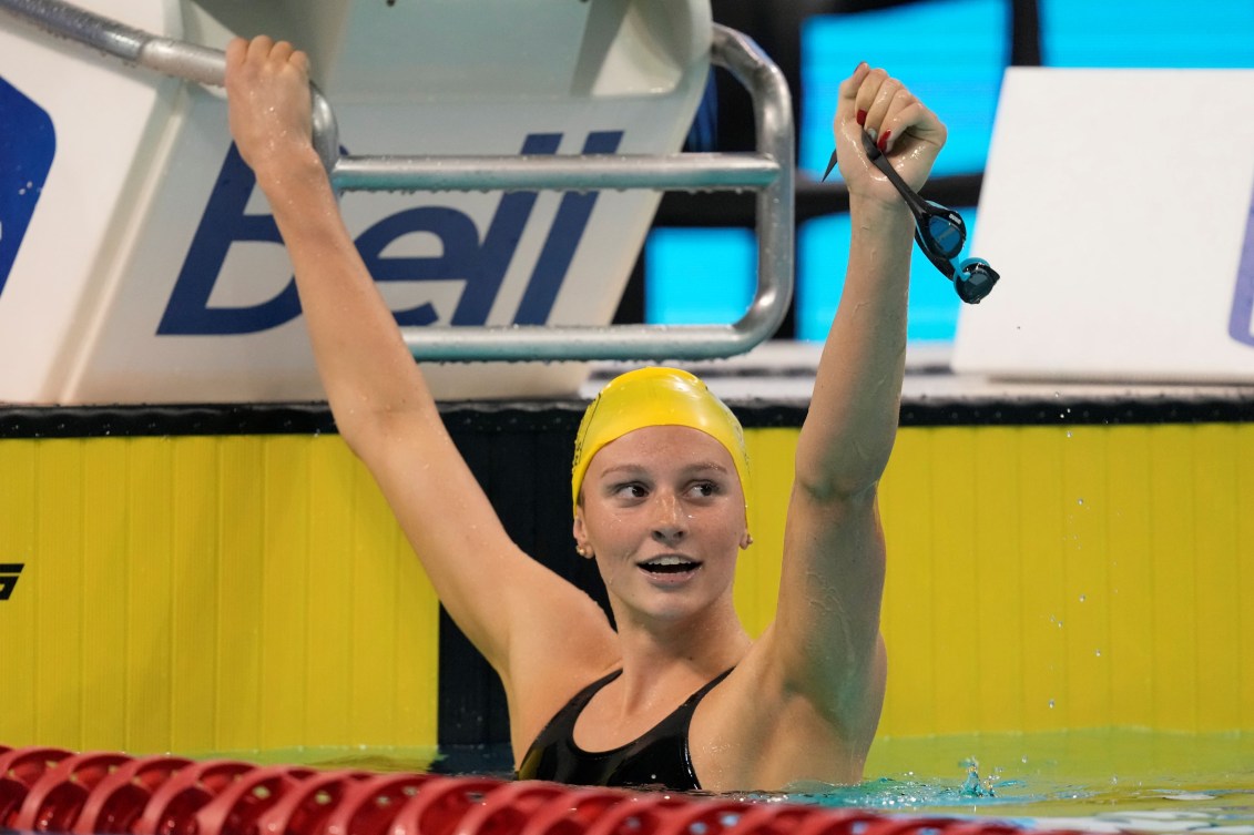 Summer McIntosh raises her arms in the air while hanging from the start blocks in the pool

