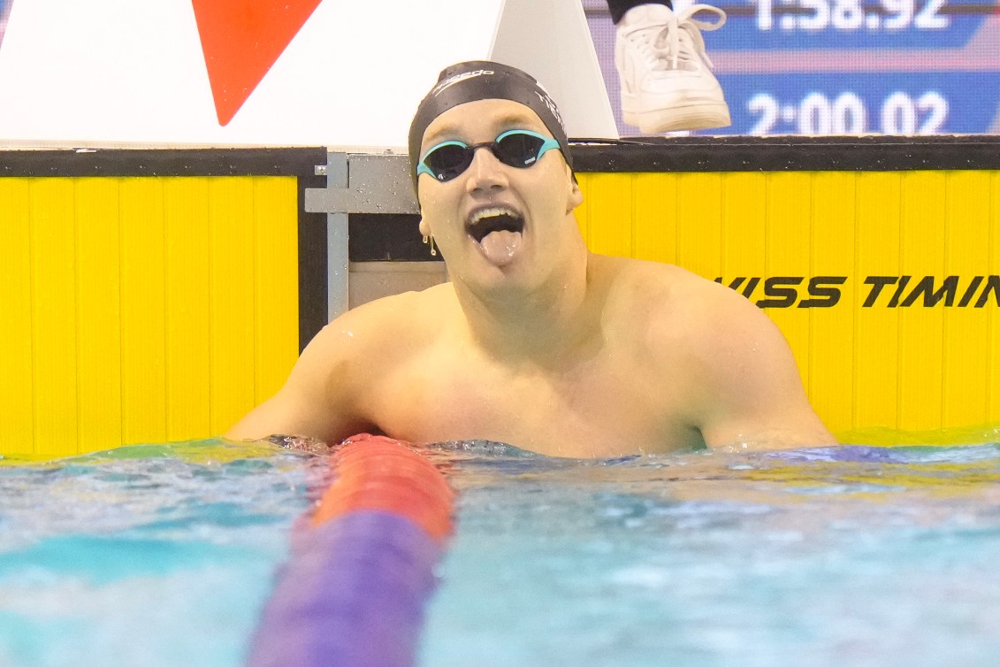 Blake Tierney sticks out his tongue as he looks at his time while hanging off the pool lane