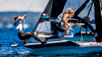 Two women hang off the edge of their racing sailboat as they compete in a regatta