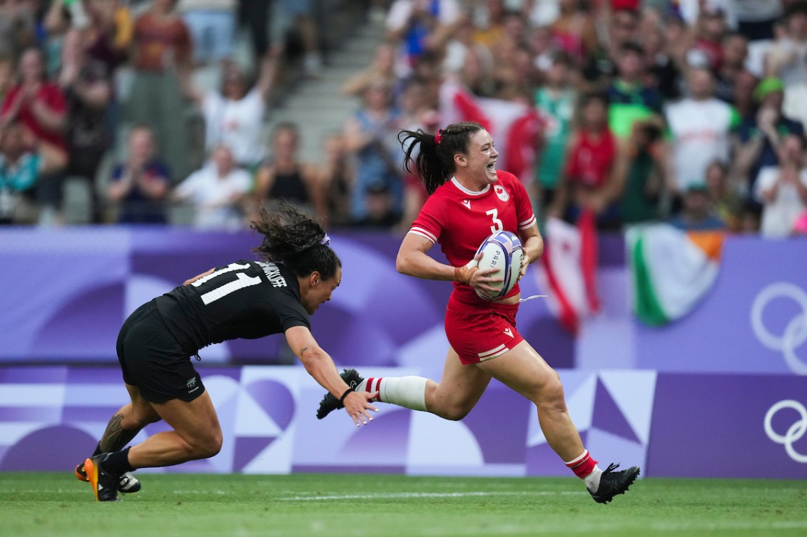 Alysha Corrigan runs with the rugby ball as a New Zealand player grabs for her foot 