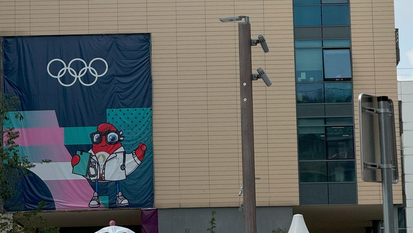 A banner of a Phryge wearing a white medical coat appears on the side of a building at the Paris 2024 Olympic Village