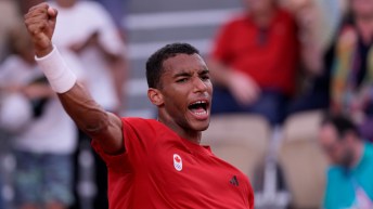 Felix Auger-Aliassime yells and pumps his fist in the air in celebration while wearing a red shirt