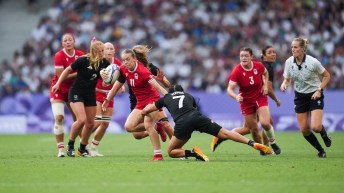 Piper Logan in red carries the ball past New Zealand players in black