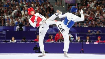 Skylar Park in a red vest and white taekwondo outfit kicks her opponent