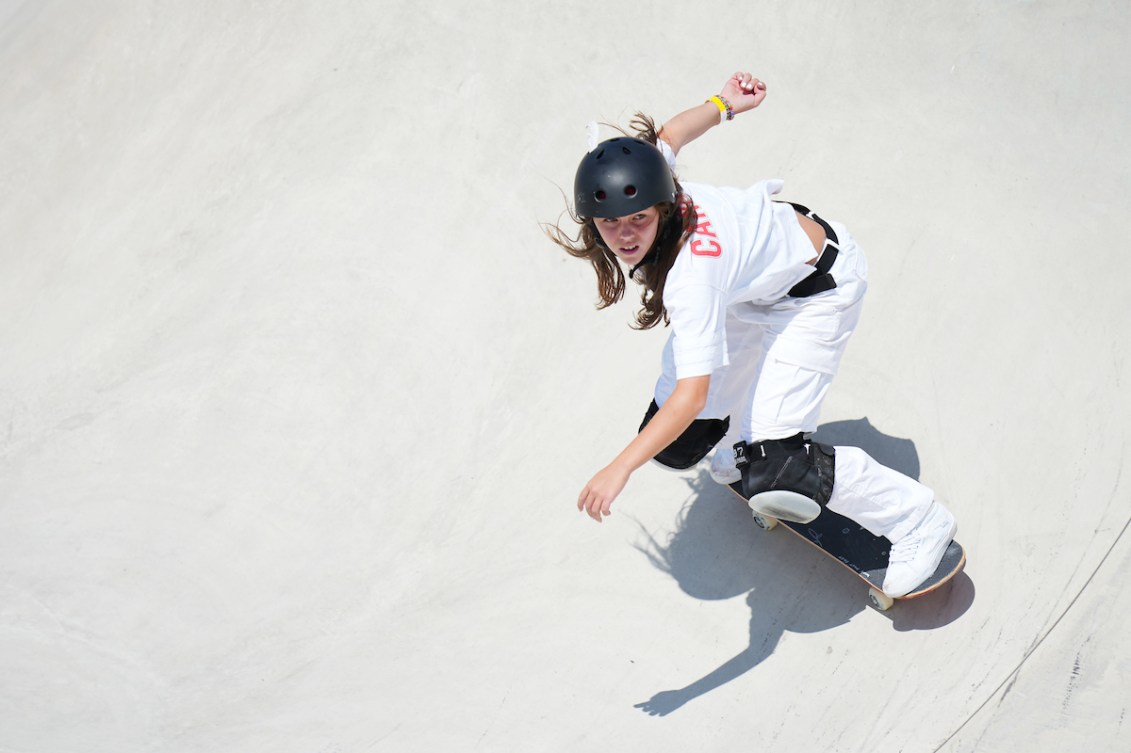 Fay De Fazio Ebert rides her skateboard while wearing an all white outfit and black helmet