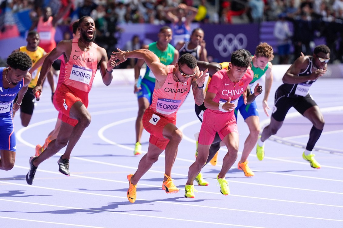 Andre De Grasse receives the baton and starts his sprint while wearing a pink singlet