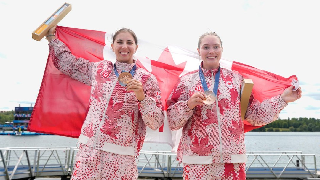 Katie Vincent and Sloan Mackenzie wear their bronze medals and hold a Canadian flag over their shoulders