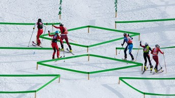 Six ski mountaineering athletes climb up a ski hill around green course markings