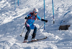 A skier dressed in blue descends on rough snow around coloured poles