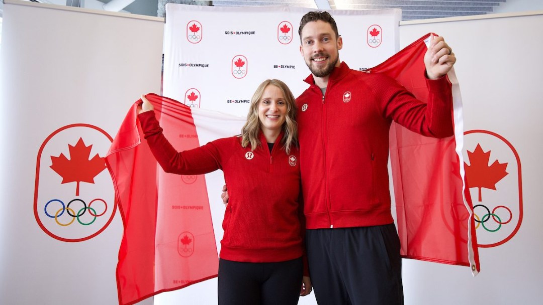 Dressed in red tops and black pants Jocelyn Peterman and Brett Gallant hold a Canadian flag behind them