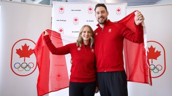 Dressed in red tops and black pants Jocelyn Peterman and Brett Gallant hold a Canadian flag behind them