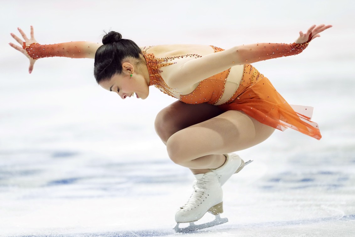 Madeline Schizas performs a sit spin while wearing an orange dress