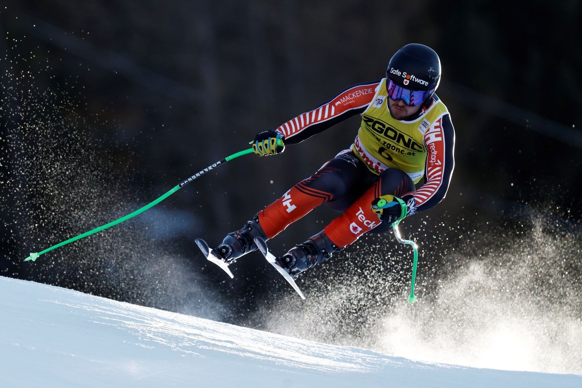 Cameron Alexander is a little airborne while skiing in a red and black suit and yellow bib