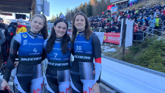 Caitlin Nash, Embyr Lee Susko and Trinity Ellis stand arm in arm beside a luge track