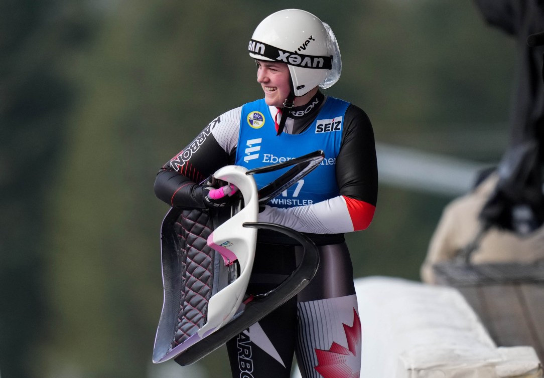Embyr Lee Susko carries her luge sled while wearing a speed suit and white helmet