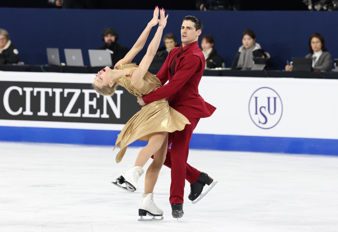 Piper Gilles in a gold dress and Paul Poirier in a red suit perform a dance spin