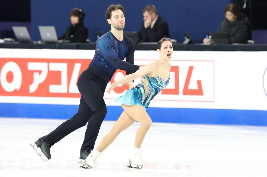 A woman in a blue turquoise dress and a man in navy blue skate in a pairs program