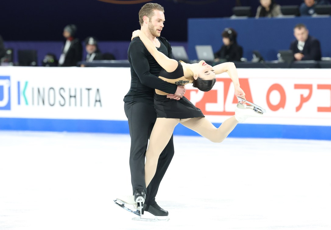 Pairs figure skaters dressed in black perform a spin