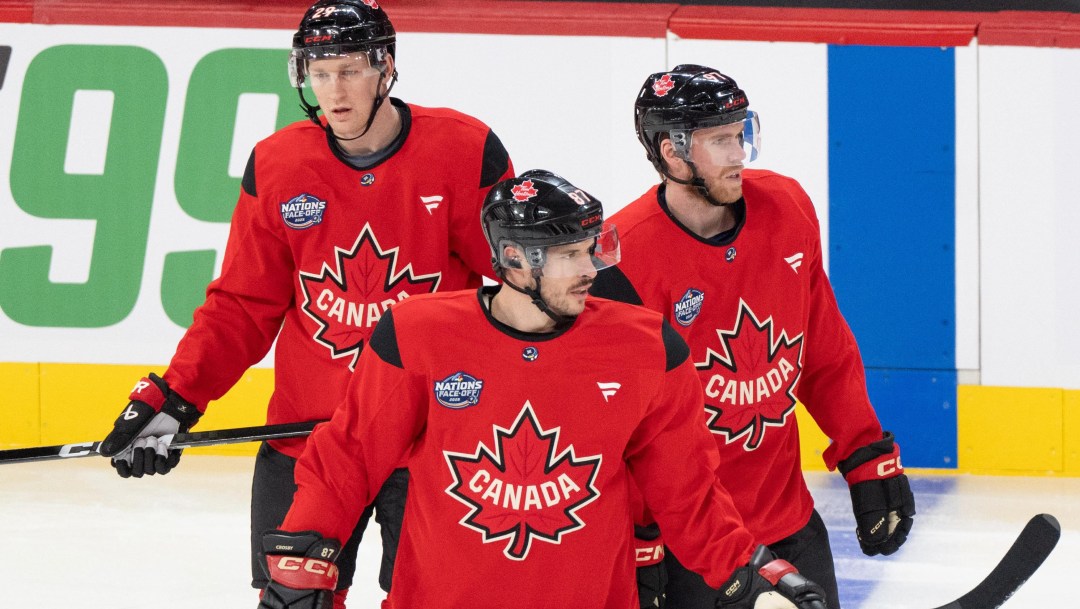 Sidney Crosby, Connor McDavid and Nathan MacKinnon stand on the ice wearing red Team Canada jerseys
