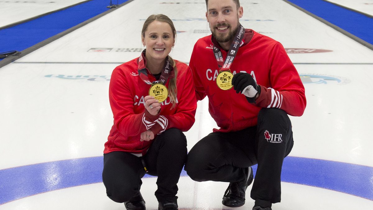 Jocelyn Peterman and Brett Gallant hold up their gold medals while crouching on the ice sheet in red jackets