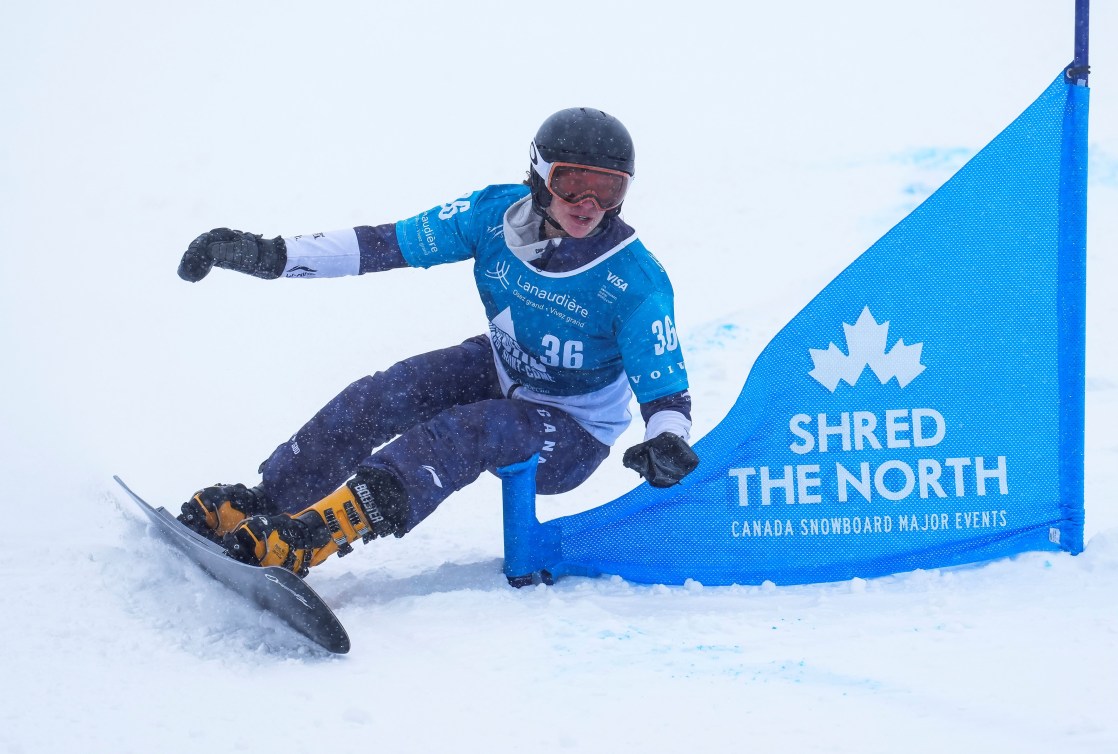 Aurelie Moisan in a blue bib snowboards past a blue flag gate