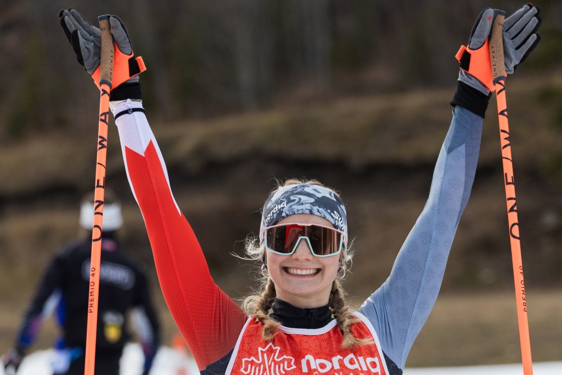 Sonjaa Schmidt lifts her poles into the air and smiles while wearing sunglasses