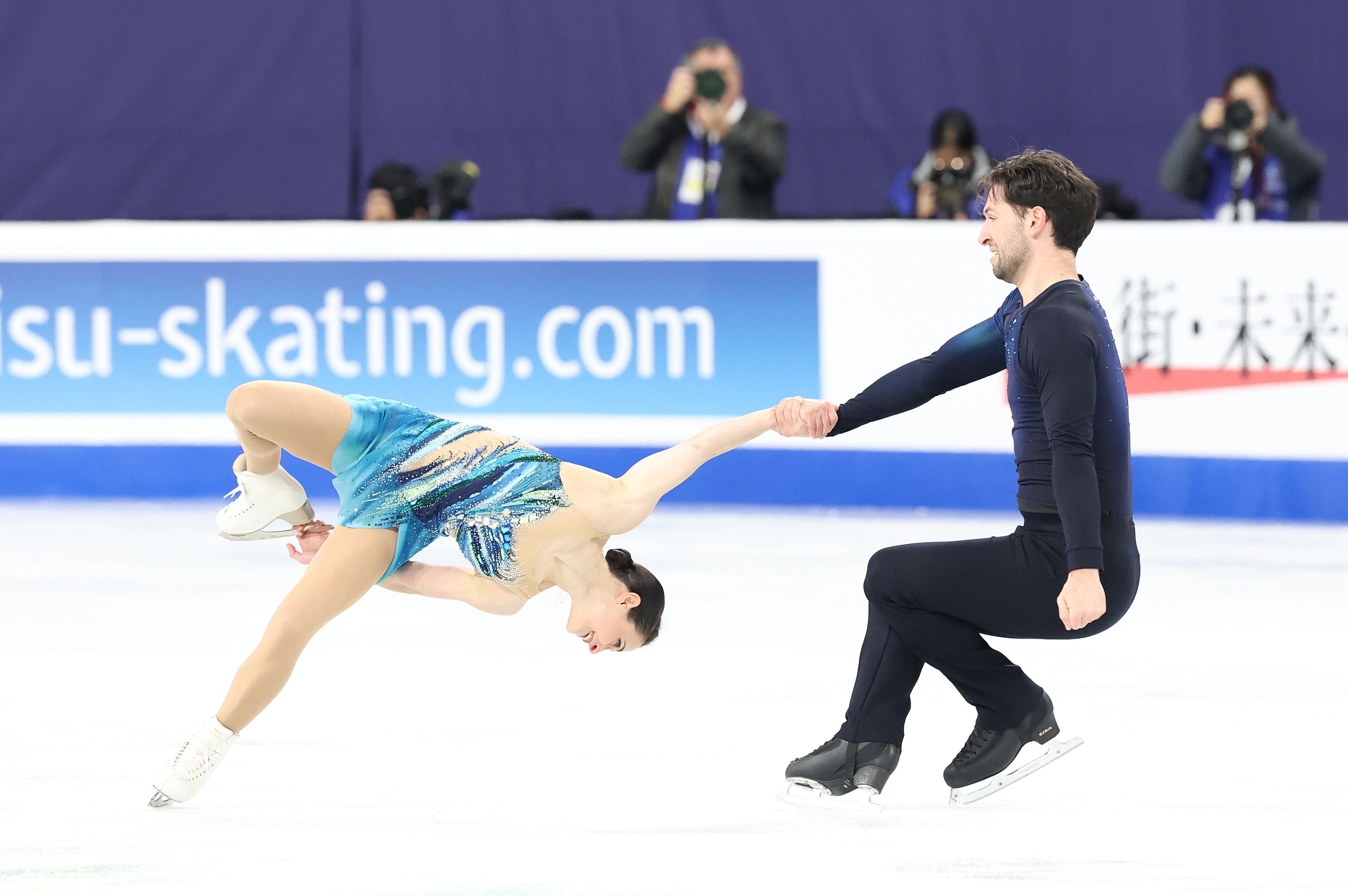 Deanna Stellato-Dudek in a multi tone blue dress performs a death spiral with partner Maxime Deschamps who is dressed in dark blue pants and shirt
