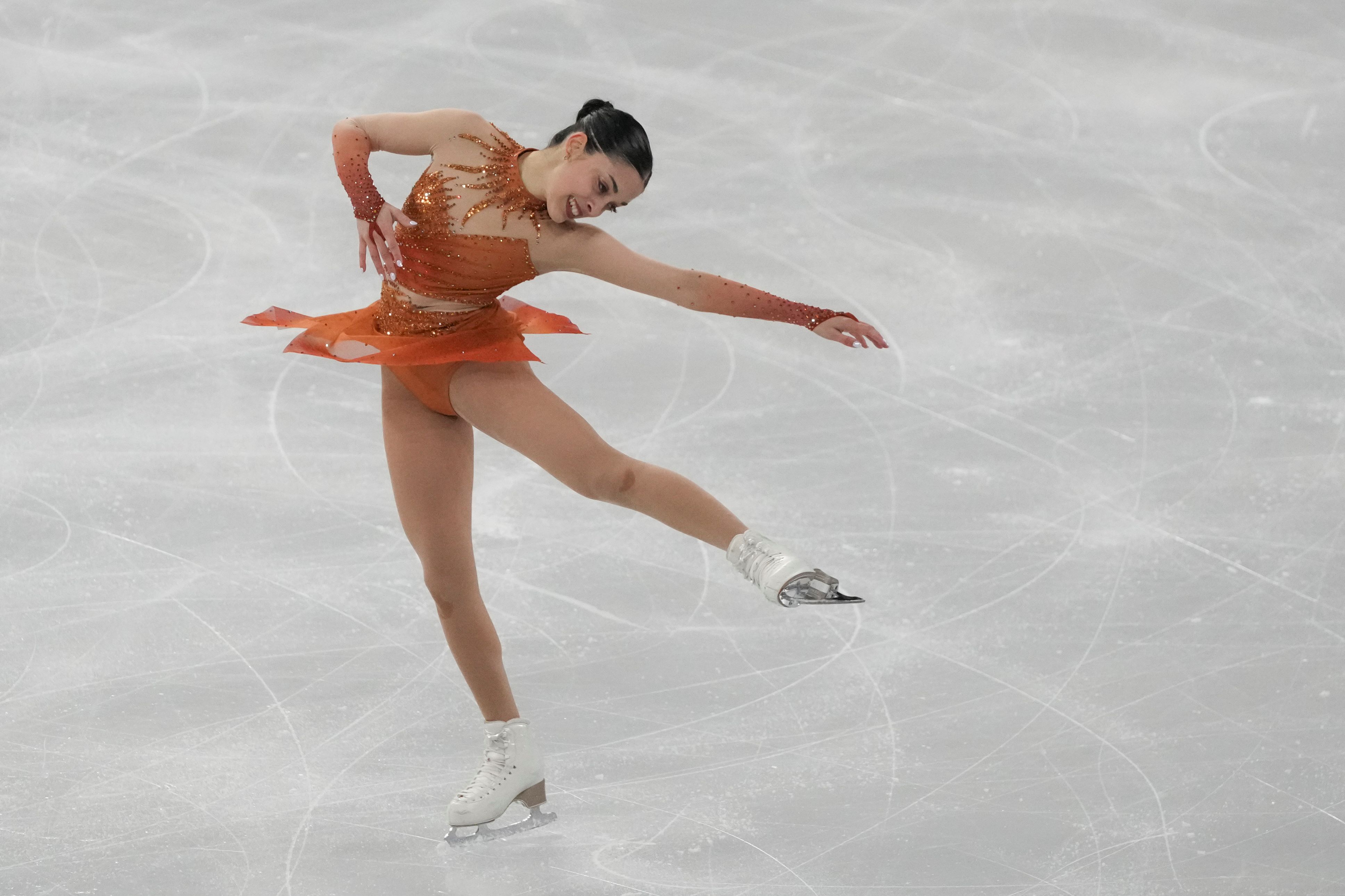 Madeline Schizas performs a layback spin in an orange dress