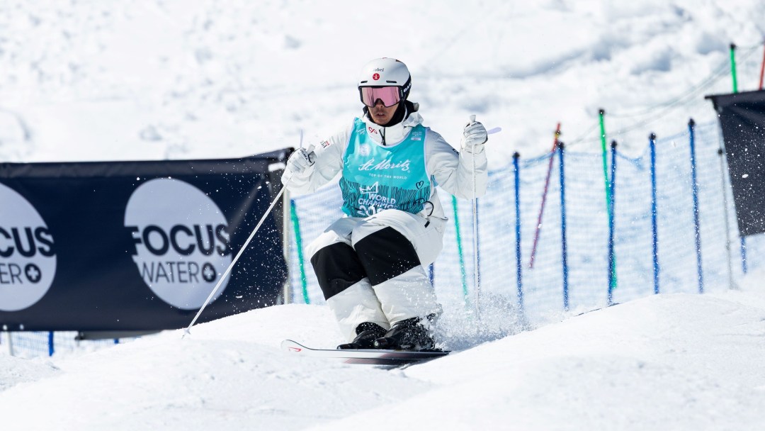 In a white snowsuit and blue bib, Mikael Kingsbury races down a moguls course