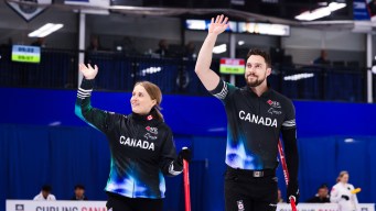 Wearing black jackets, Jocelyn Peterman and Brett Gallant wave to the crowd while smiling