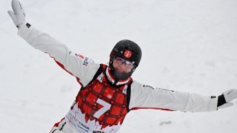 Wearing a red plaid bib over a white snowsuit, Marion Thenault smiles after landing a jump