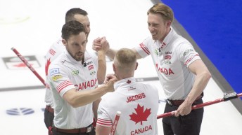 Dressed in white shirts, the four members of the Canadian men's curling team shake hands with each other