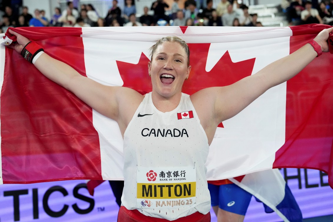Sarah Mitton holds a Canada flag above her shoulders while wearing a white singlet
