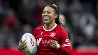 Asia Hogan-Rochester smiles and carries the rugby ball while wearing a red jersey
