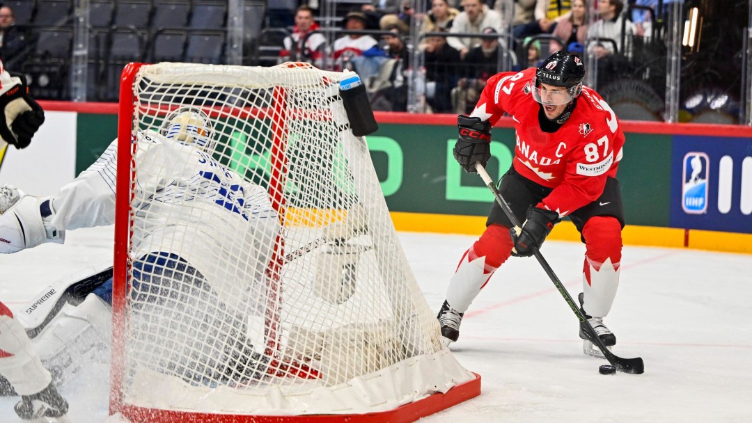 Sidney Crosby plays the puck behind the next while wearing a red Team Canada jersey