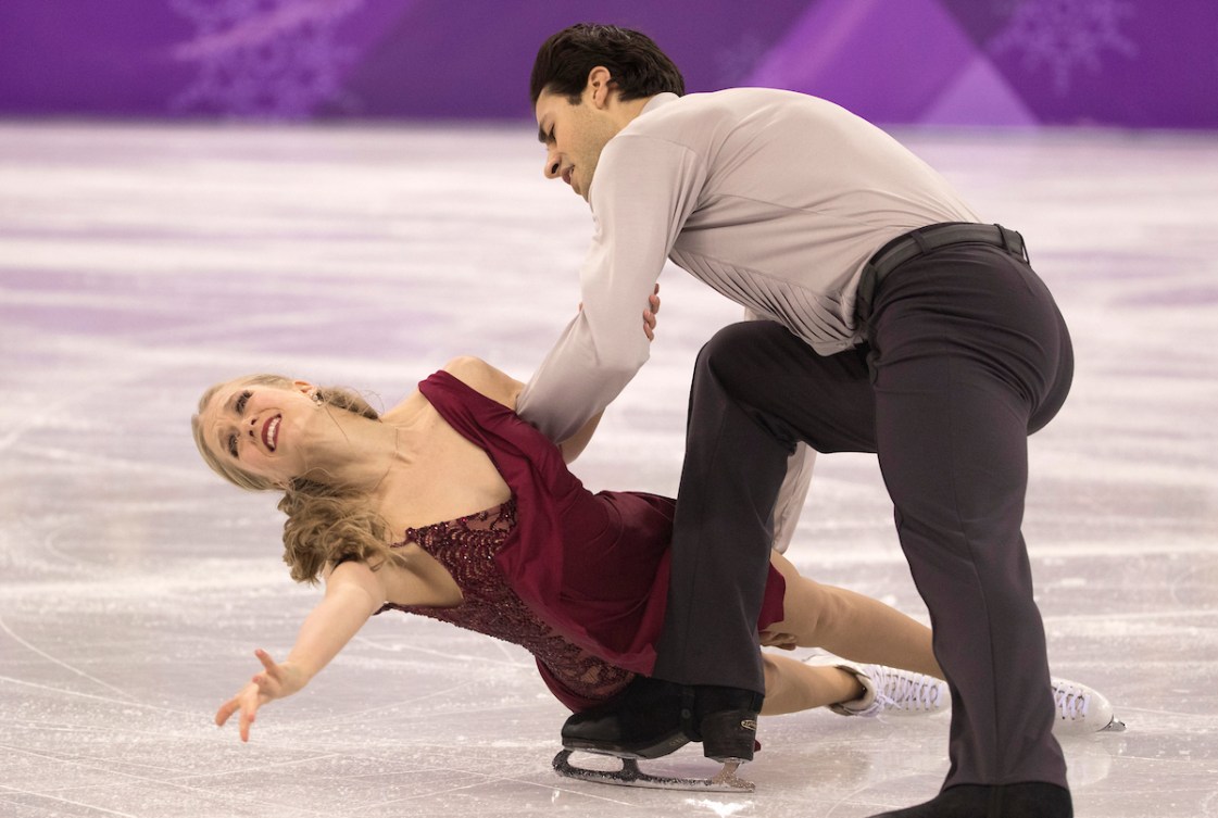 Kaitlyn Weaver in a red dress does a hydroblade move with partner Andrew Poje dressed in a grey shirt and black pants
