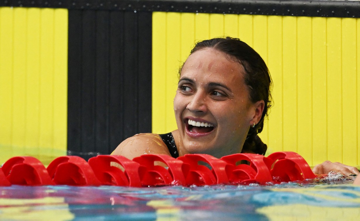 Kylie Masse hangs onto the red lane rope at the end of the pool while smiling 