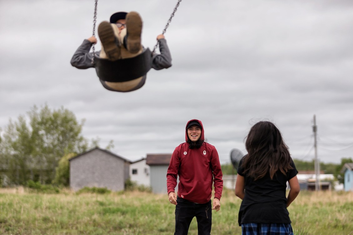 Liam Gill pushes a child on the swings while wearing a red sweater